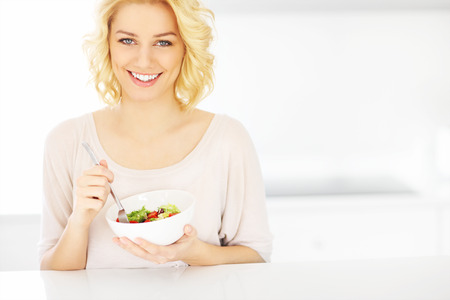 A picture of a young woman eating salad in the kitchenの写真素材