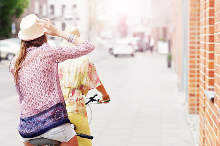 A picture of two girl friends riding a tandem bicycle in the cityの写真素材