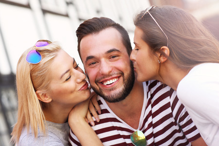 A picture of two attractive women kissing a man in the cityの写真素材