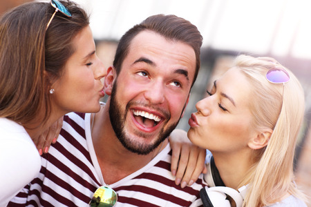 A picture of two attractive women kissing a man in the cityの写真素材