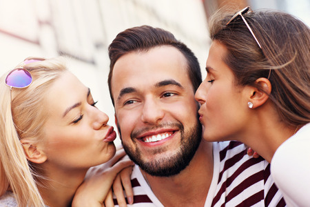 A picture of two attractive women kissing a man in the cityの写真素材