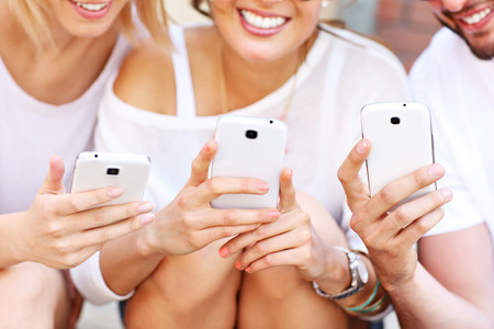 A picture of a group of friends using smart phones in the cityの写真素材
