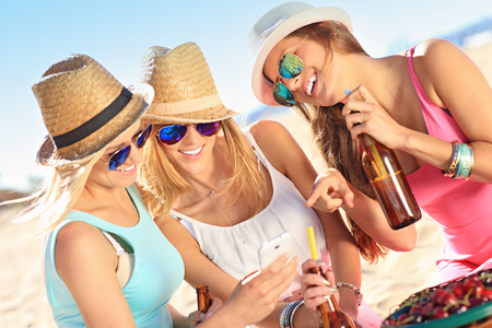 A picture of a group of friends drinking beer and texting on the beachの写真素材