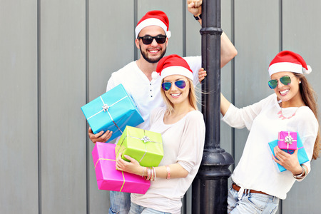 A picture of group of friends in Santa's hats sitting in the city with presentsの写真素材