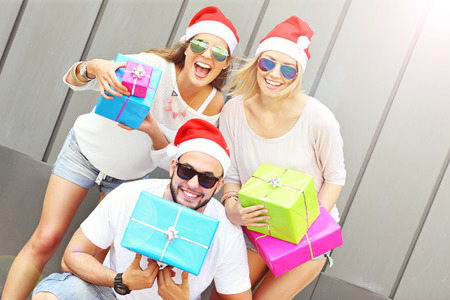A picture of group of friends in Santa's hats sitting in the city with presentsの写真素材