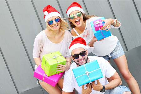 A picture of group of friends in Santa's hats sitting in the city with presentsの写真素材