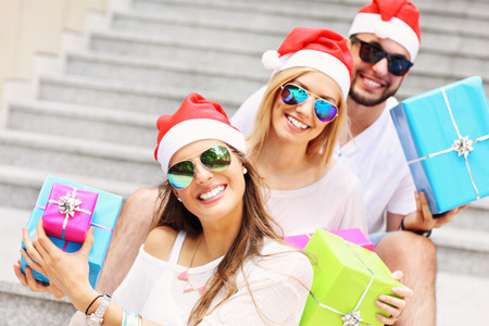 A picture of group of friends in Santa's hats sitting in the city with presentsの写真素材