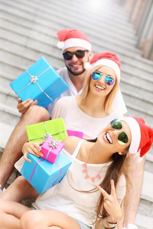 A picture of group of friends in Santa's hats sitting in the city with presentsの写真素材
