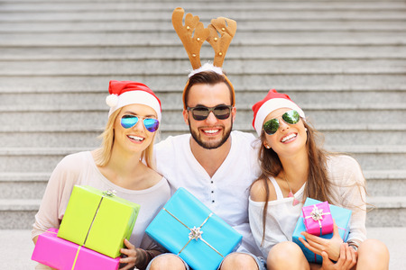A picture of group of friends in Santa's hats sitting in the city with presentsの写真素材