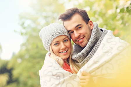 A picture of a young romantic couple covered with blanket in the park in autumnの写真素材