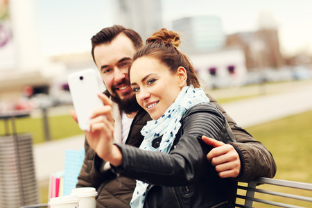 Picture of young couple sitting with shopping bags and smartphoneの写真素材