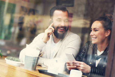 Picture of happy couple using phones in restaurantの写真素材