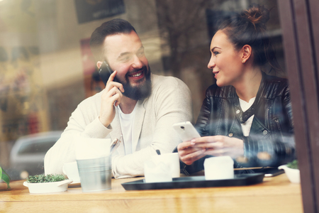 Picture of happy couple using phones in restaurantの写真素材