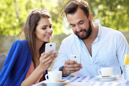 Picture of young couple using cellphone in a restaurantの写真素材