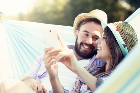 Picture of romantic couple using smartphone in hammockの写真素材