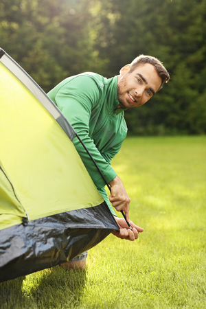 Picture of young man putting up tent in the forestの写真素材