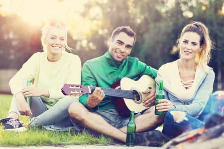 Picture showing couple camping in forest and playing guitarの写真素材