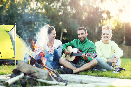 Picture showing couple camping in forest and playing guitarの写真素材