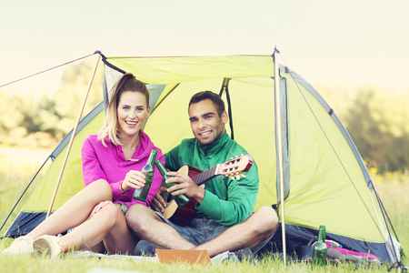 Picture showing couple camping in forest and playing guitarの写真素材