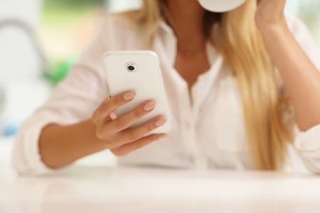 Midsection of young woman in the kitchen with smartphoneの写真素材
