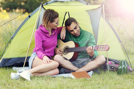 Picture showing couple camping in forest and playing guitarの写真素材