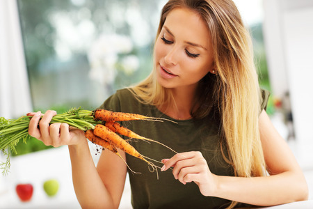 Picture of young woman with fresh carrots in kitchenの写真素材