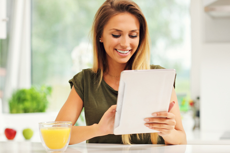 Picture of young woman with orange juice and tablet in kitchenの写真素材