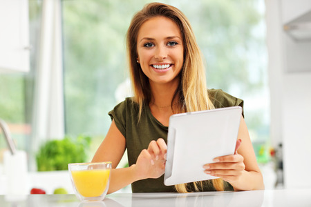 Picture of young woman with orange juice and tablet in kitchenの写真素材