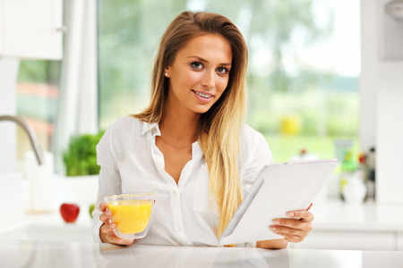 Picture of young woman with orange juice and tablet in kitchenの写真素材