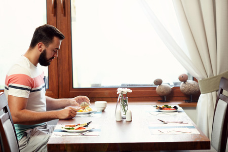 Picture of young man sitting alone at hotel restaurant table and eating breakfastの写真素材