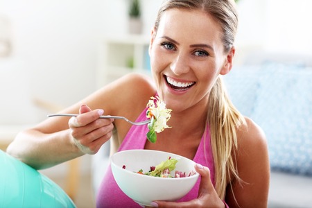 Young woman eating healthy salad after workoutの写真素材