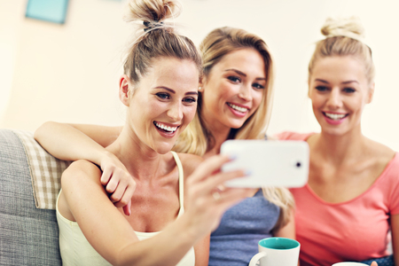 Three beautiful young women chilling at home and taking selfieの写真素材