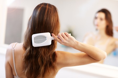 Young woman standing in bathroom and brushing hairの写真素材