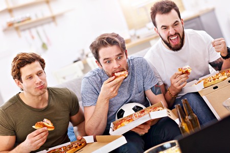 Happy male friends eating pizza and watching tvの写真素材