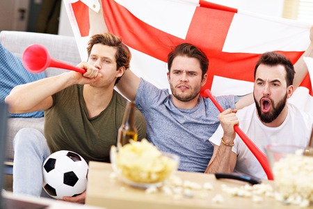 Happy male friends cheering and watching sports on tvの写真素材