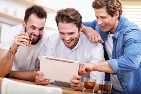 Cheerful friends having fun with smartphone and drinking at homeの写真素材