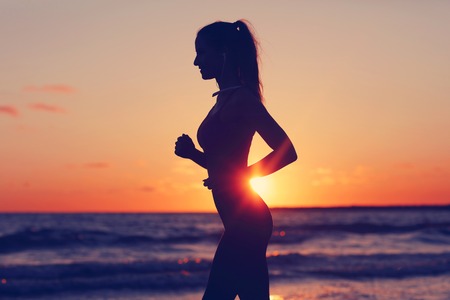Woman running alone at beautiful dusk on the beachの写真素材