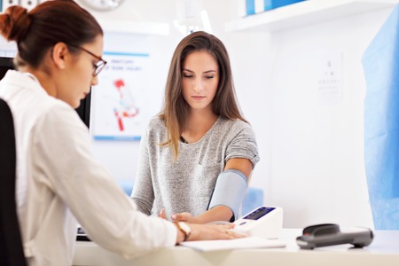 Adult woman having blood pressure test during visit at female doctors officeの写真素材
