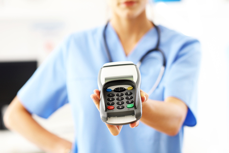 Female doctor standing in her office with payment terminal