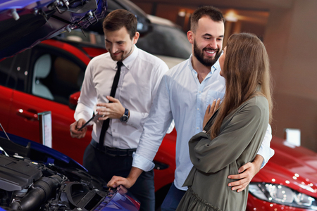 Confident young salesman explaining car features to the young attractive owners