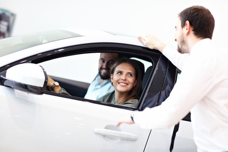 Confident young salesman explaining car features to the young attractive owners