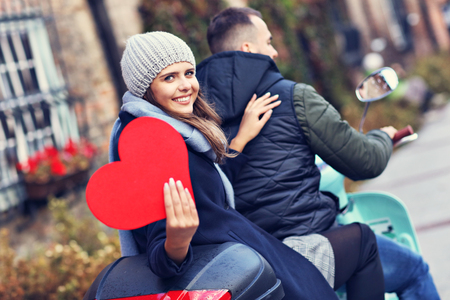 Beautiful young couple holding hearts while riding scooter in city in autumnの写真素材