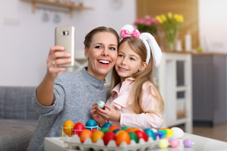 Mother and daughter painting Easter eggs and taking selfieの写真素材