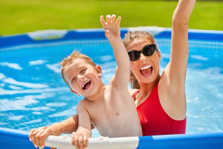 Picture of cute boy with his mother playing in a pool of water during the summerの写真素材