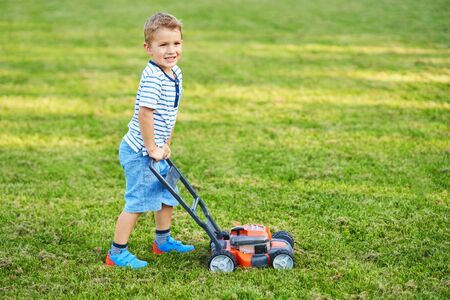 Happy 3 year old boy having fun mowing lawnの写真素材