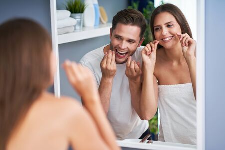 Portrait of happy young couple flossing teeth in the bathroomの写真素材