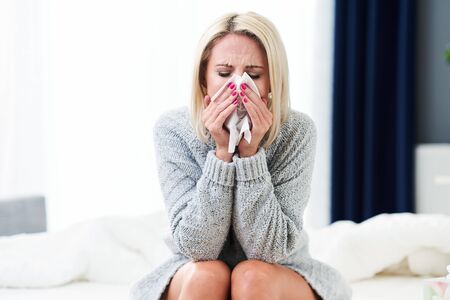 Adult woman feeling unwell with runny nose at homeの写真素材