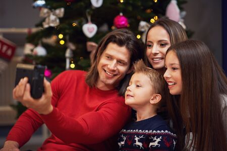 Beautiful family celebrating Christmas at home and taking instant picturesの写真素材