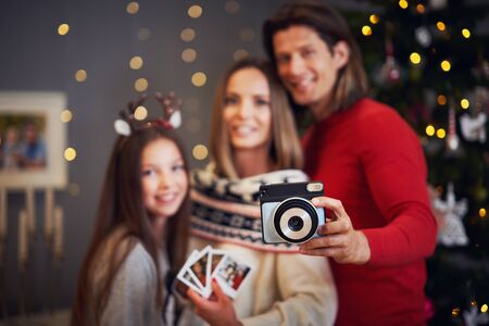 Beautiful family celebrating Christmas at home and taking instant picturesの写真素材