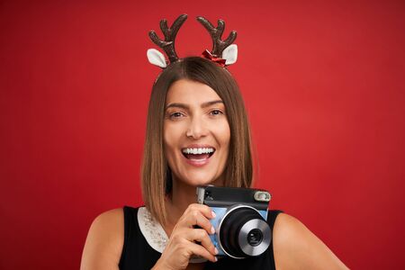 Adult happy woman in Christmas mood taking instant pictures over red background